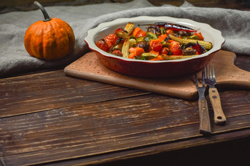 Delicious vegetables baked in the oven on a ceramic plate on a wooden table. Devices, fabric and...