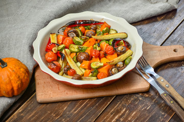 Delicious vegetables baked in the oven on a ceramic plate on a wooden table. Devices, fabric and accessories. Copy space.