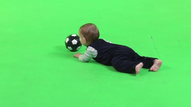 Sweet little baby boy playing with a small ball, crawling on the floor over a green screen.