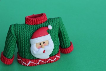 Fototapeta premium green and red resin sweater with Santa Claus wearing hat and beard standing on a green background with writing space