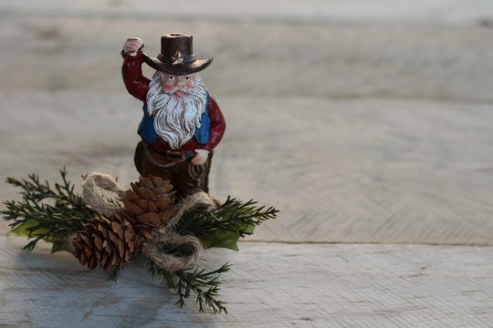 cowboy Santa Claus with beard standing next to pine cones and pine branches on a natural wood background with writing space