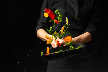 Professional cook. He prepares a dish with vegetables in a saucepan. on black background, menu,...