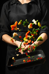 The chef prepares the vegetables on the pan. Black background for copying text. Restaurant business and advertising.