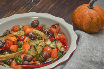Rural still life of grilled vegetables and in a large ceramic plate and appliances on a wooden background. Copy space.