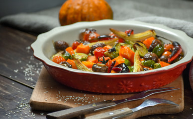 Rural still life of grilled vegetables and in a large ceramic plate and appliances on a wooden background. Copy space.