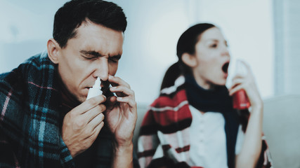 Sick Couple Sitting on Sofa in Checkered Blankets.