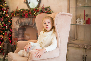 Obraz na płótnie Canvas Christmas portrait of happy blonde child girl in white sweater siting on the floor near the Christmas tree. New Year Holidays