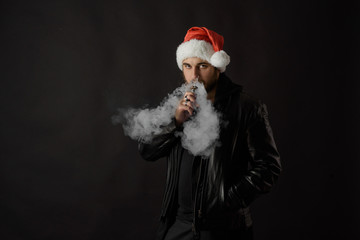 Man with beard in Santa red hat smoking electronic sigarette. vape pen. vape smoke. Christmas...