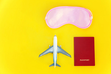 Flat Lay with plane, sleeping eye mask and passport on yellow colourful trendy modern fashion background. Vacation travel summer weekend sea adventure trip concept