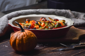 Rural still life of grilled vegetables and in a large ceramic plate and appliances on a wooden background. Copy space.
