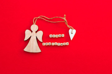 Christmas wooden angel with heart and twine with words Merry Christmas on little bricks on bright red background. Minimalism concept. Natural eco materials New Year toy.  Top view. Postcard template
