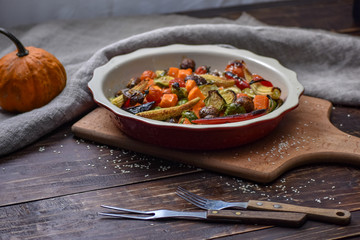 Rural still life of grilled vegetables and in a large ceramic plate and appliances on a wooden background. Copy space.
