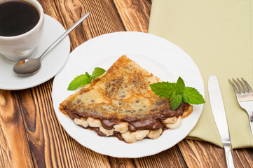 Crepes with bananas and cream on a wooden background