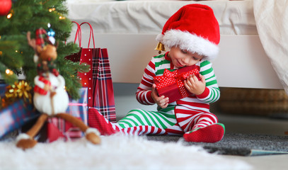 happy baby boy  in pajamas with gifts on christmas morning near   tree