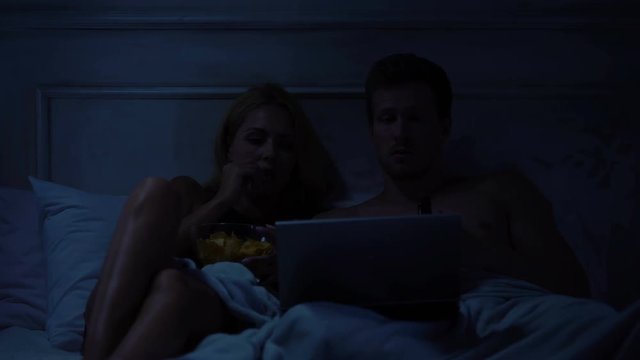 Couple watching psychological thriller on laptop, eating snacks, scary movie