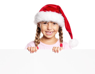 Portrait of happy little girl in Santa hat with white blank. Child wearing Santa Claus hat, posing behind white panel. Kid holding empty Christmas billboard, peeping behind blank holidays board. 