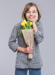 Holidays, love, hapiness and people concept - happy child celebrating Valentines day. Beautiful teen girl with flowers. Funny cute girl with bouquet of yellow tulips on gray background. 