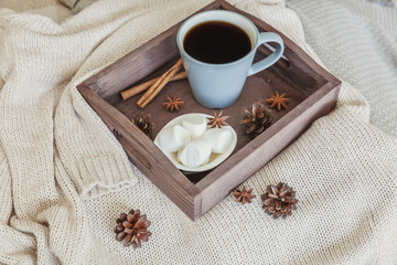 Cup of coffee on rustic wooden tray, sweet marshmallow and warm woolen sweater. Cozy autumn or winter weekend or holidays at home. Fall home decoration with hot drink mug. Hygge morning style concept