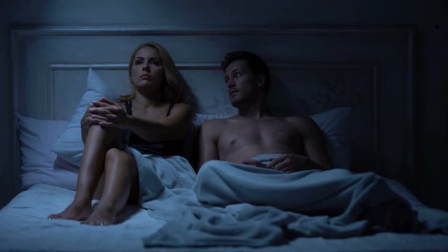 Couple quarreling in bed, male trying to apologize, lady pushing him away