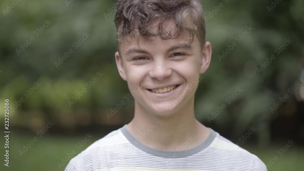 Wall mural Close up emotional portrait of caucasian smiling teen boy. Handsome guy. Funny cute teenager in summer park at day. Child looking at camera.