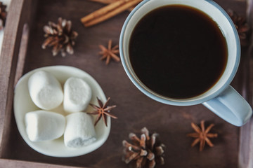 Cup of coffee on rustic wooden tray, sweet marshmallow and warm woolen sweater. Cozy autumn or winter weekend or holidays at home. Fall home decoration with hot drink mug. Hygge morning style concept