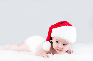 very beautiful bright emotional happy little baby in Santa hat crawling on white plaid