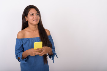 Studio shot of young happy Indian woman smiling while thinking a