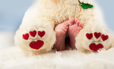 small tender legs of the baby, together with the paws of a Teddy bear with hearts on a white blanket