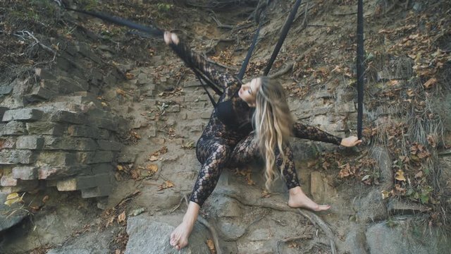 A beautiful blond girl in a body stocking tied with black ribbons to the roots is trying to free herself. Modern and fashion performance.