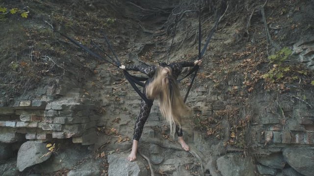 A beautiful blond girl in a body stocking tied with black ribbons to the roots is trying to free herself. Modern and fashion performance.