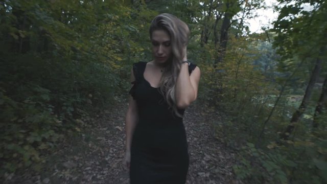 A beautiful girl in a black dress walks along a forest autumn road.
