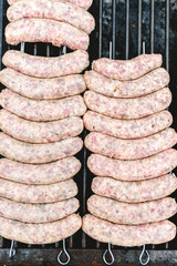 Many white sausages in a row to roast on a barbecue with charcoal.