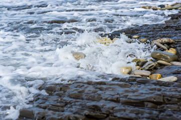 pebble stones on the sea beach, the rolling waves of the sea with foam