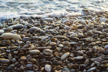 pebble stones on the sea beach, the rolling waves of the sea with foam