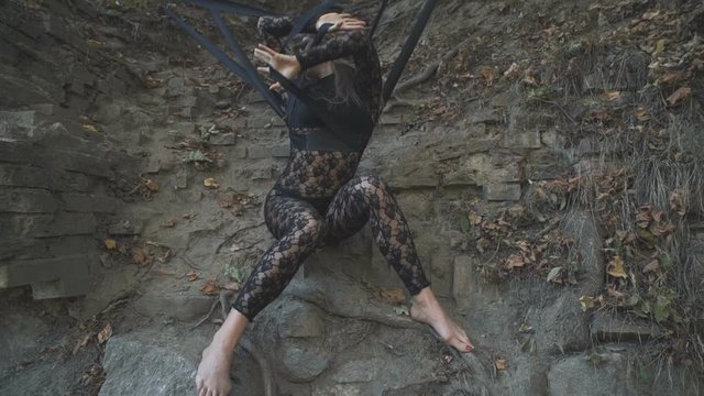 A beautiful blond girl in a body stocking tied with black ribbons to the roots is trying to free herself. Modern and fashion performance.