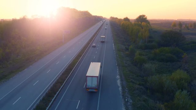 Aerial following shot of a semi trucks with cargo trailer moves on the suburban highway at sunset