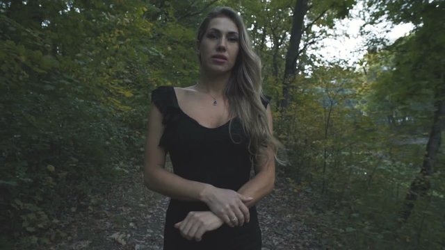 A beautiful girl in a black dress walks along a forest autumn road.