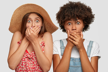 Photo of speechless surprised young women stare at camera with eyes popped out, cover mouthes,...