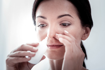 Self treatment. Close up of pleasant woman dripping her nose and looking down