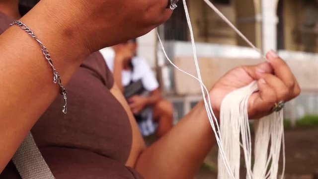 Filipino woman belonging to marginal earners prepares cotton strings thread to make candle wick at the side of the street