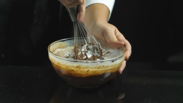 Making bakery chocolate cake. Whipping liquid chocolate with a whisk with the addition of milk in a thin stream on a black background