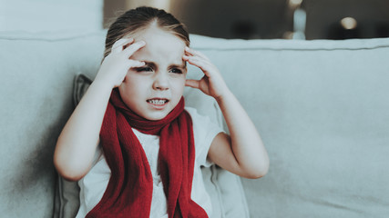 Little Girl with Cold Sitting on Sofa in Red Scarf