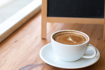 A white cup of hot coffee on wooden table,A refreshment before work time or refreshment in relaxing time in a break with empty black board for write menu in coffee shop