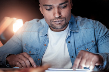 Completing task. Handsome international male person bowing head and pressing lips while looking at tablet