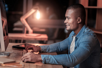 Finally did. Delighted male person leaning arms on the table and typing document while sitting in semi position