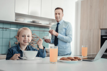 Morning and breakfast. Joyful cute pleasant girl sitting in the kitchen by the table smiling and eating.