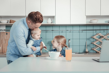 Obraz premium Little happiness. Attentive caring lovely father standing in the kitchen near his daughter hugging and holding little baby.
