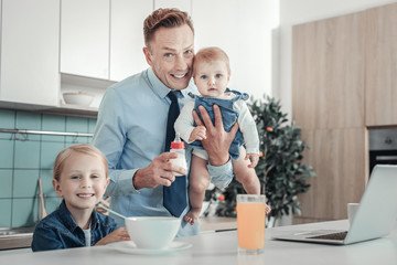 We are happy. Satisfied handsome lovely father holding a baby smiling and spending time with...