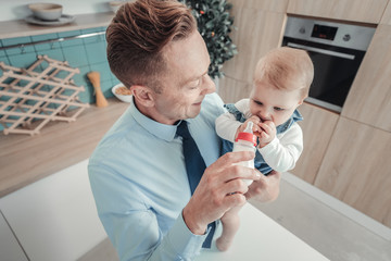 Try this. Careful smiling responsible man standing in the kitchen holding a bottle of milk and...