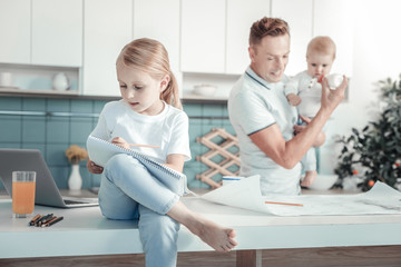 Fototapeta premium Important notes. Concentrated busy little girl sitting in the bright room on the table writing and focusing on this task.